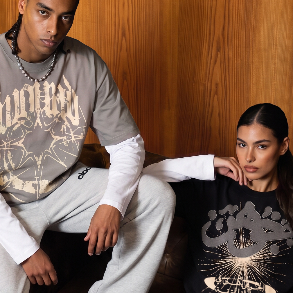 Two models in Clocal Wound and Gawhar tees on a leather sofa